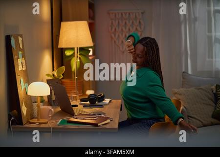 Tired Black Woman Stretching at Desk While Working Late from Home Stock Photo