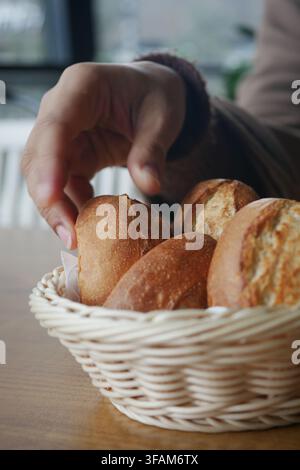 Hand reaching for bread rolls in a basket Stock Photo