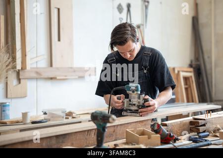 Focused professional master restorer working in restoration workshop with electric wood router. Stock Photo