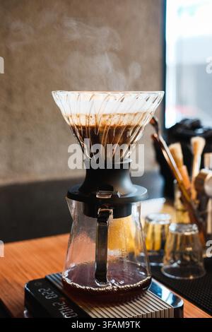Fresh coffee brewing in a glass V60 dripper with visible steam on a wooden counter at a specialty cafe. Manual pour over process. Stock Photo