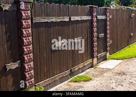 Rustic wooden gate with dark timber planks and sturdy brick pillars creating a charming entrance to a private countryside estate with a textured grave Stock Photo