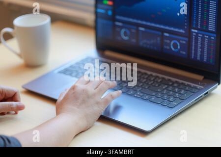 Hands working on a laptop displaying financial data, with coffee on desk. Concept of online trading, data analysis, remote work, and modern digital bu Stock Photo