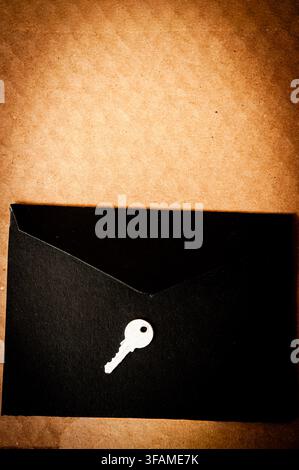 Black envelope with a small white key on a brown textured background, conceptual image of secrecy, access, mystery and confidential information Stock Photo