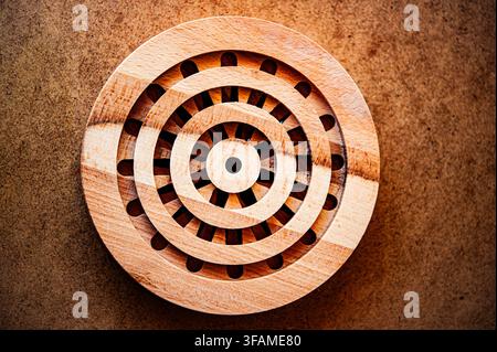 Top view of a circular layered wooden puzzle with radial slots on a brown textured surface, highlighting geometric craft and natural wood grain Stock Photo