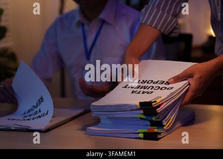 Hands placing stack of financial report documents on desk for working late workload Stock Photo