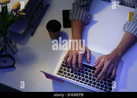Top down view of hands typing on laptop working late at desk Stock Photo