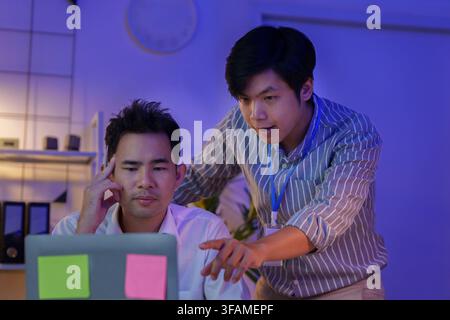 Asian business colleagues working late at night in office collaborating on laptop Stock Photo