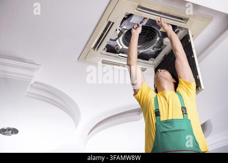 The young mechanic repairs the ceiling air conditioner Stock Photo