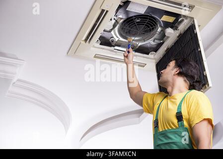 Young mechanic repairs ceiling air conditioner Stock Photo
