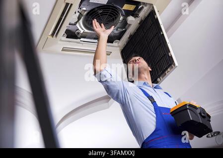 Young mechanic repairs ceiling air conditioner Stock Photo