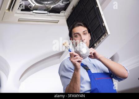 Young mechanic repairs ceiling air conditioner Stock Photo