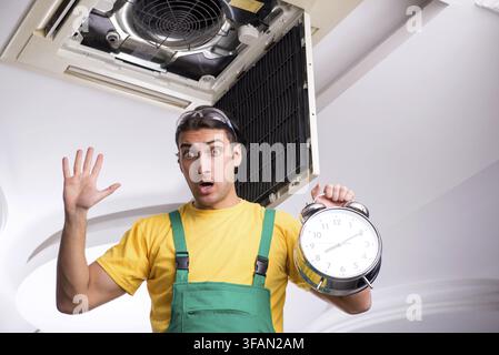 Young mechanic repairs ceiling air conditioner Stock Photo