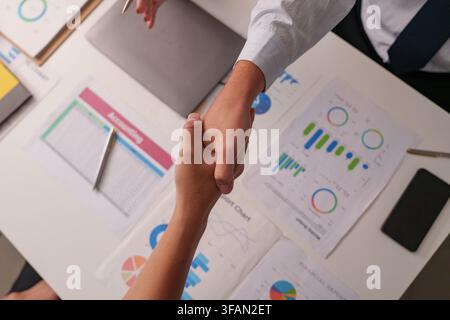 Overhead view of business partners shaking hands over financial report documents on desk Stock Photo
