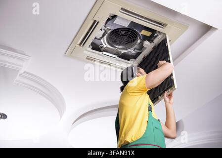 The young mechanic repairs the ceiling air conditioner Stock Photo