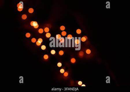 Abstract dark background featuring glowing orange bokeh light spots creating a creative festive pattern against a black backdrop. Stock Photo