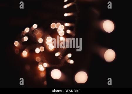 Abstract background featuring glowing blurred lights creating soft bokeh circles and warm festive illumination glowing in the dark. Stock Photo