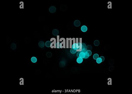 Abstract background featuring glowing cyan bokeh light circles floating in the dark with soft blur effects and vibrant colors. Stock Photo