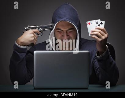 Young hooded man sits in front of a laptop and plays and commits suicide Stock Photo