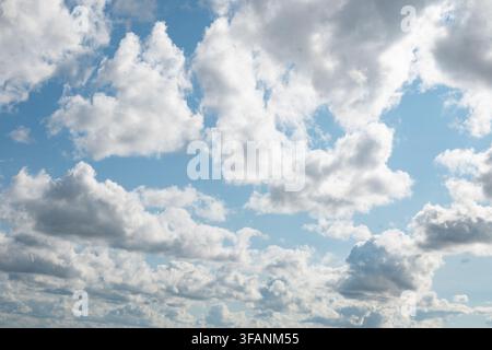 A bright blue sky filled with puffy white clouds and small fluffy formations. The gentle sunlight and clear weather create a calm and serene daytime l Stock Photo