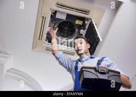 Young mechanic repairs ceiling air conditioner Stock Photo