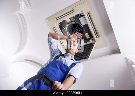 The young mechanic repairs the ceiling air conditioner Stock Photo