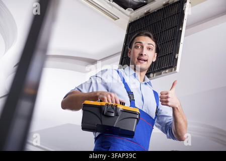 Young mechanic repairs ceiling air conditioner Stock Photo