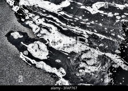 Frothy soapy waste water from window cleaner's bucket poured out across pavement making an abstract monochrome - Tours, Indre-et-Loire (37), France. Stock Photo