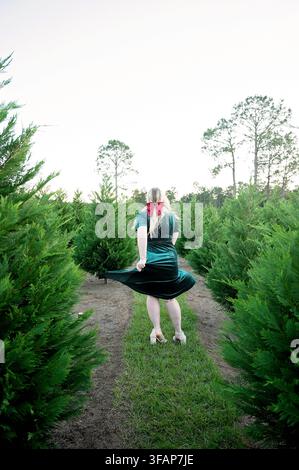 Woman in green dress twirls at a tree farm Stock Photo