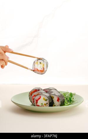 Woman holding a fresh sushi roll with chopsticks Stock Photo