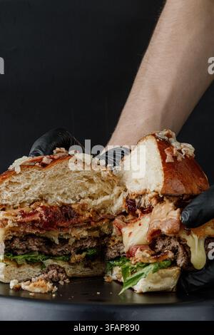 Hands in gloves hold a huge messy burger cut open Stock Photo