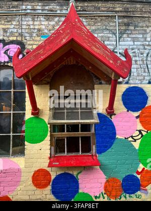Freetown Christiania street art with a red pagoda-style window awning and vibrant polka dot graffiti on a brick wall in Copenhagen, Denmark. Stock Photo