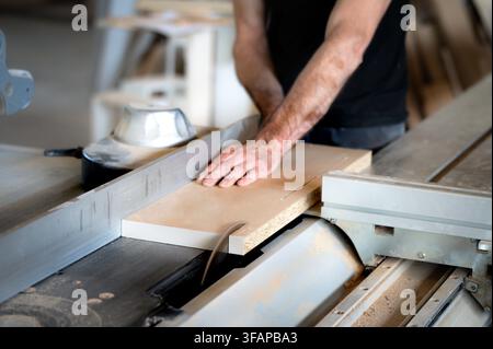 Worker skillfully pushing wood through a table saw in a busy workshop Stock Photo