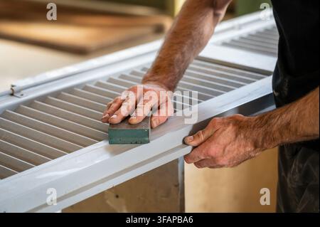 Worker preparing wooden shutter for painting with a sanding block in a workshop Stock Photo