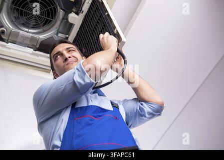 Young mechanic repairs ceiling air conditioner Stock Photo