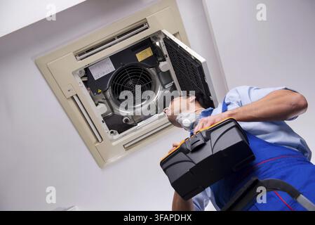 Young mechanic repairs ceiling air conditioner Stock Photo