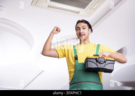 Young mechanic repairs ceiling air conditioner Stock Photo