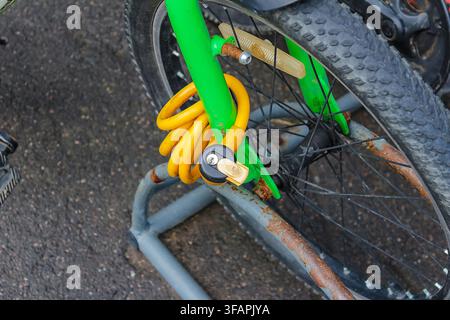A partial view of a bicycle secured to a metal stand with a yellow curved lock. Focus is on the frame, lock, and part of the wheel Stock Photo