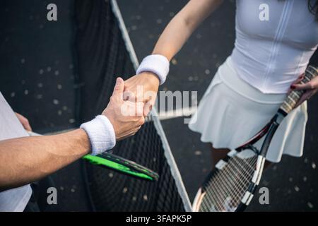Close up of male and female tennis players shaking hands over the net, showing sportsmanship, respect and fair play after an outdoor match. Stock Photo