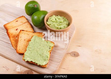 Fresh avocado fruits, avocado spread and avocado toast on pale beige wooden kitchen Stock Photo