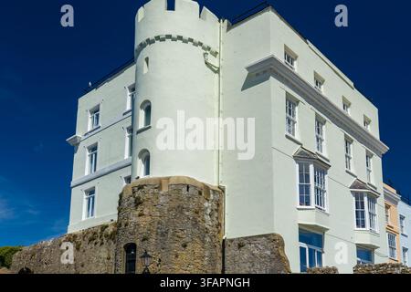 Castle Hill House built atop medieval stone town walls in Tenby, Wales, showing white painted facade with crenellated round turret under a clear blue Stock Photo