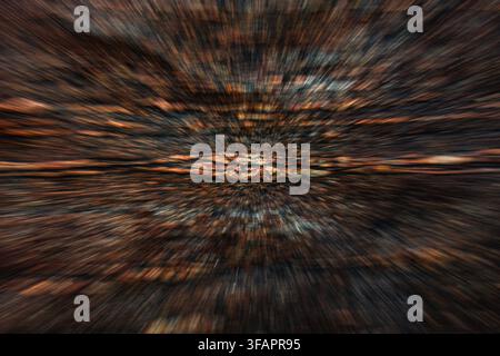 A radial zoom-burst motion effect capturing an orange forest floor covered in fallen leaves, creating a dynamic starburst pattern. Stock Photo