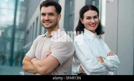 Two happy Caucasian business colleagues male with female with crossed hands looking at camera smiling in city. Cheerful man with woman businessman Stock Photo