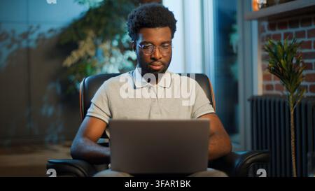 Serious African American business man working laptop at evening at home office overworked businessman male guy user work online with computer network Stock Photo