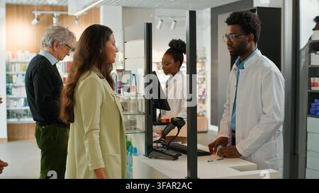 Indian young woman and old Caucasian man clients buying pills in pharmacy talking with African American pharmacists sellers working in drugstore Stock Photo