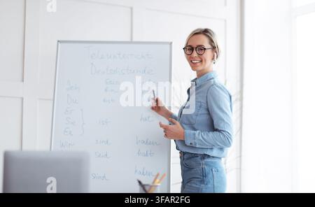 Happy young teacher standing near blackboard and explaining German lesson to students online from home, panorama Stock Photo