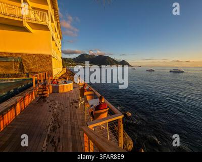 Evening light reflects on water as people relax and boats drift at sunset in a coastal setting near mountains Stock Photo