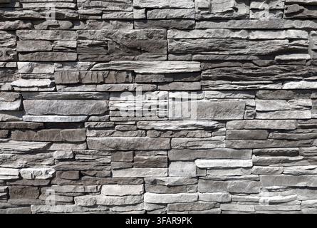 Stone coating wall made of striped stacked slabs of gray and black rocks.  Background and texture. Stock Photo