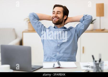 Guy Holding Hands Behind Head Sitting At Laptop In Office Stock Photo