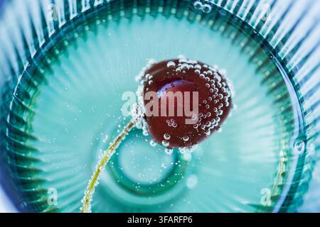 Top view macro of a fresh cherry floating in sparkling water with delicate bubbles, creating a clean abstract composition for wellness branding, bever Stock Photo