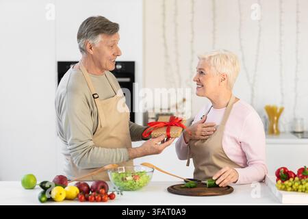 Aged Husband Giving Gift To Wife In Kitchen At Home Stock Photo